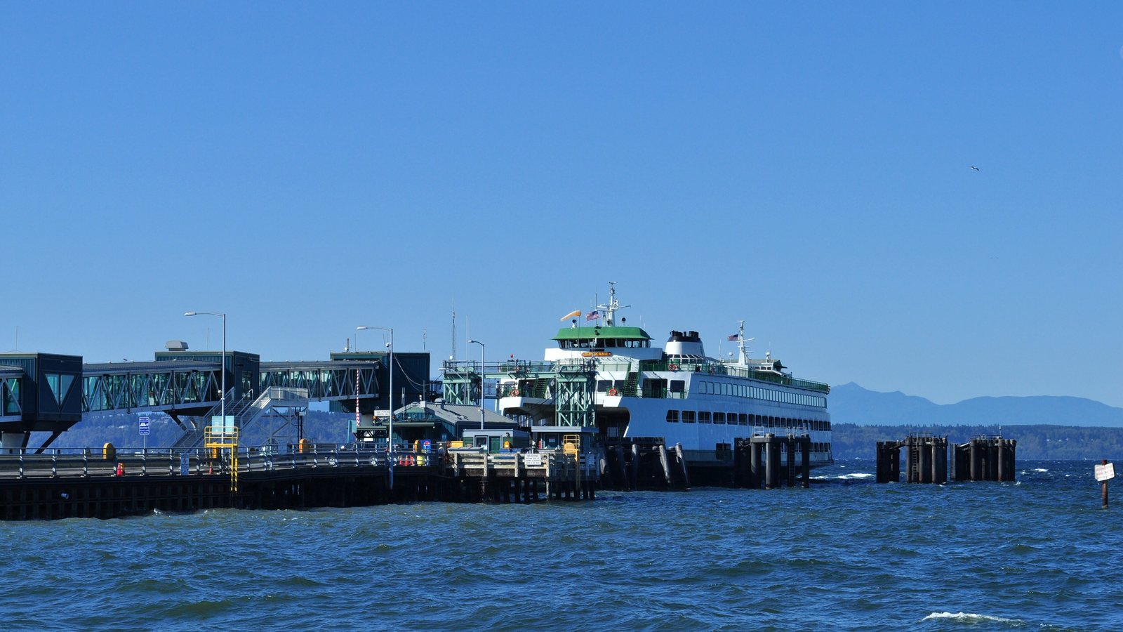 The Washington State Ferries vessel Spokane docked at the Edmonds ferry terminal, with the overhead passenger walkway and the Olympic Mountains behind